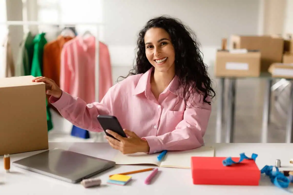 Profesional autónoma gestionando pedidos y usando un smartphone en su espacio de trabajo.