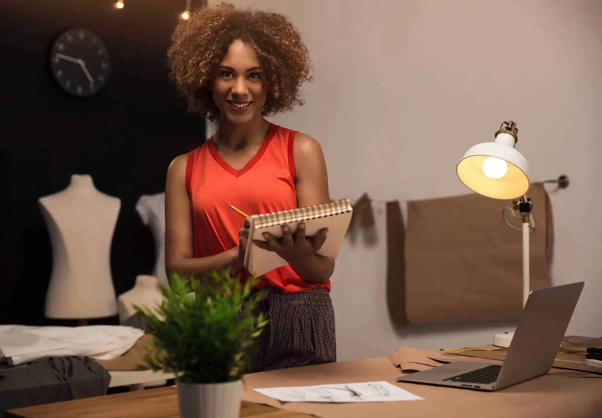 Diseñadora de moda trabajando en su estudio con un cuaderno y un portátil, creando diseños únicos para su marca de ropa.